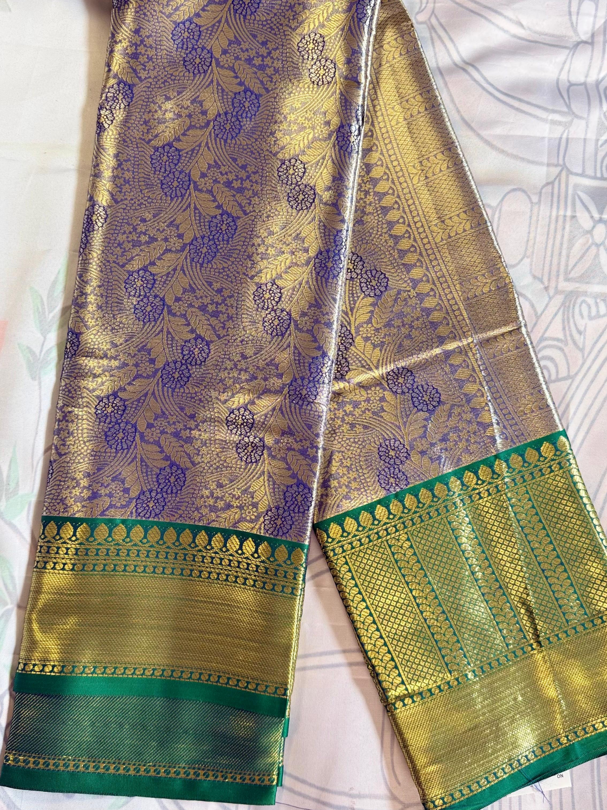 Gold and green traditional fabric with intricate patterns on a white background